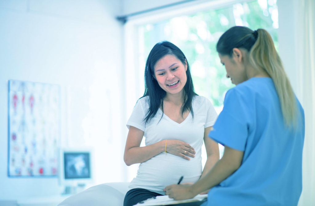 Nurse writing on clipboard while talking with a pregnant woman