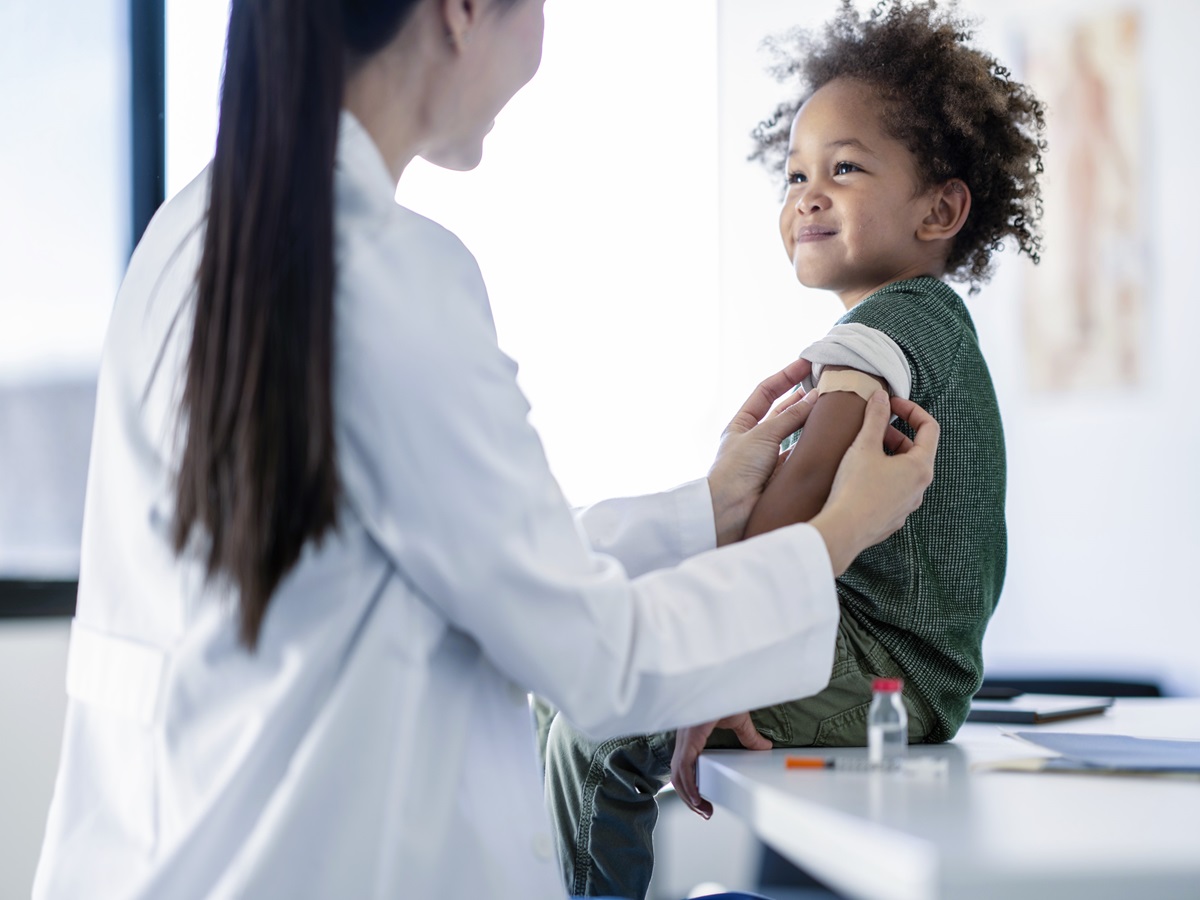 A young boy smiles as a female places a bandage on his arm